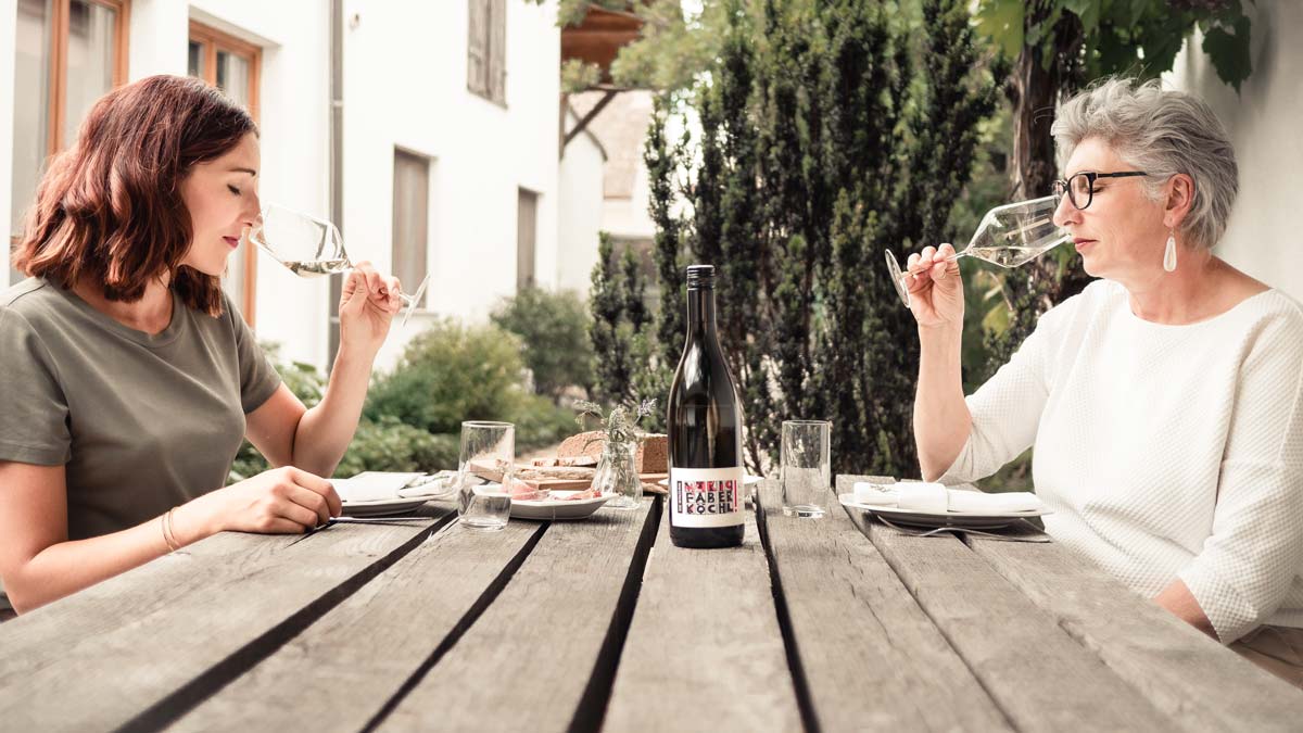 Anna Faber und Maria Faber-Köchl sitzen an einem Tisch und riechen mit geschlossenen Augen an einem Glas Wein