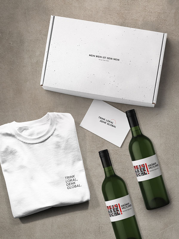 Geschenkbox mit zwei Flaschen Grüner Veltliner Saazen sowie T-Shirt und Geschenkkarte mit Aufschrift "Trink Lokal Denk Global"