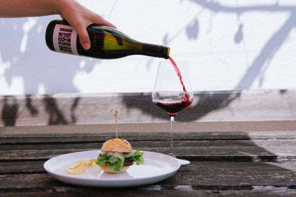 Blunzn-Burger mit einem Glas Rotwein, das gerade eingeschenkt wird