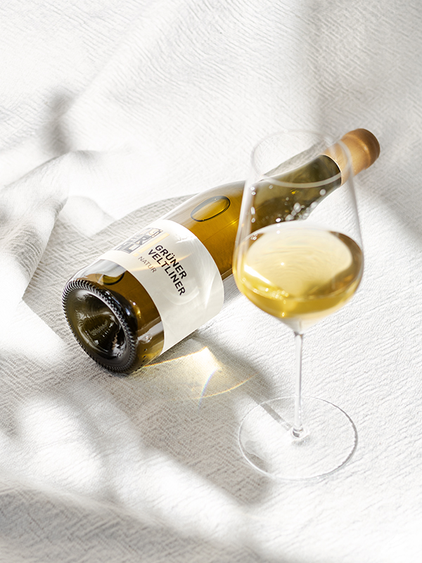 Grüner Veltliner Natur vom Weingut Faber-Köchl: Flasche liegt neben einem Bordeaux-Glas mit goldgelbem Wein