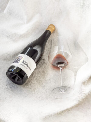 Eine Flasche der Rotwein-Cuvée Köchl Verzeichnis Exklusiv vom Weingut Faber-Köchl liegend auf einer weißen Decke, daneben liegt ein Glas Rotwein
