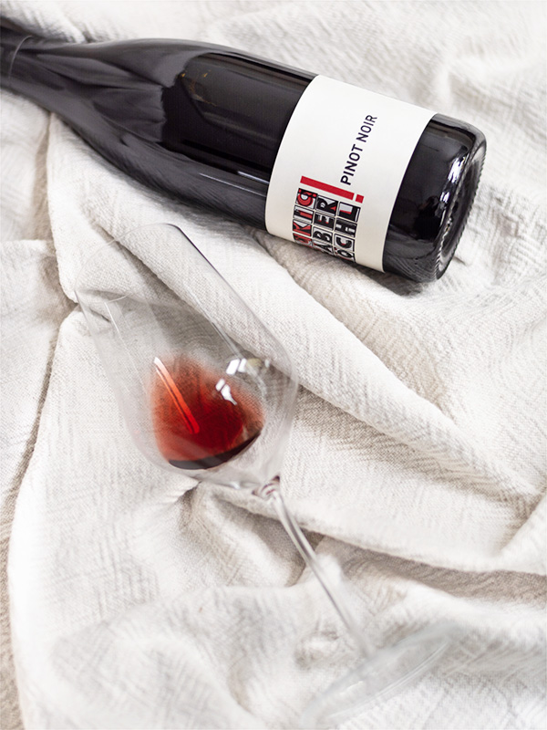 Liegende Flasche Pinot Noir vom Weingut Faber-Köchl neben einem liegenden Glas mit eingeschenktem Rotwein