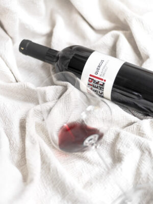 Liegende Flasche der Rotwein-Cuvée Quercus mit liegendem Glas auf weißem Hintergrund