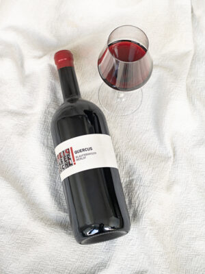 Magnum-Flasche Quercus liegt auf weißem Tuch, daneben steht ein Rotwein-Glas