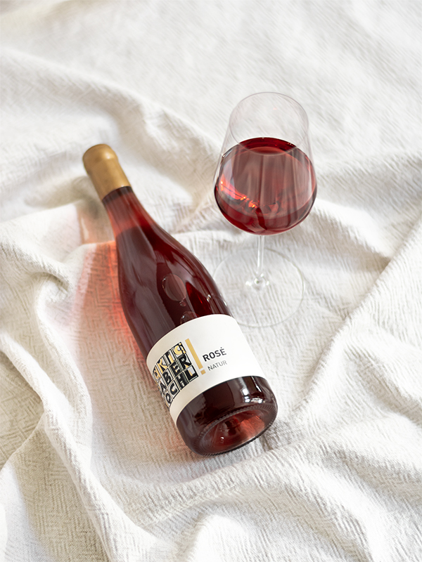 Eine Flasche Rosé Natural Wine mit einem eingeschenkten Glas auf weißem Hintergrund