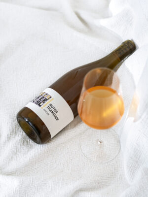 Kräftige orangegelbe Weinfarbe im Achterl-Glas, daneben liegt eine Flasche Grüner Veltliner Natur auf weißem Tuch